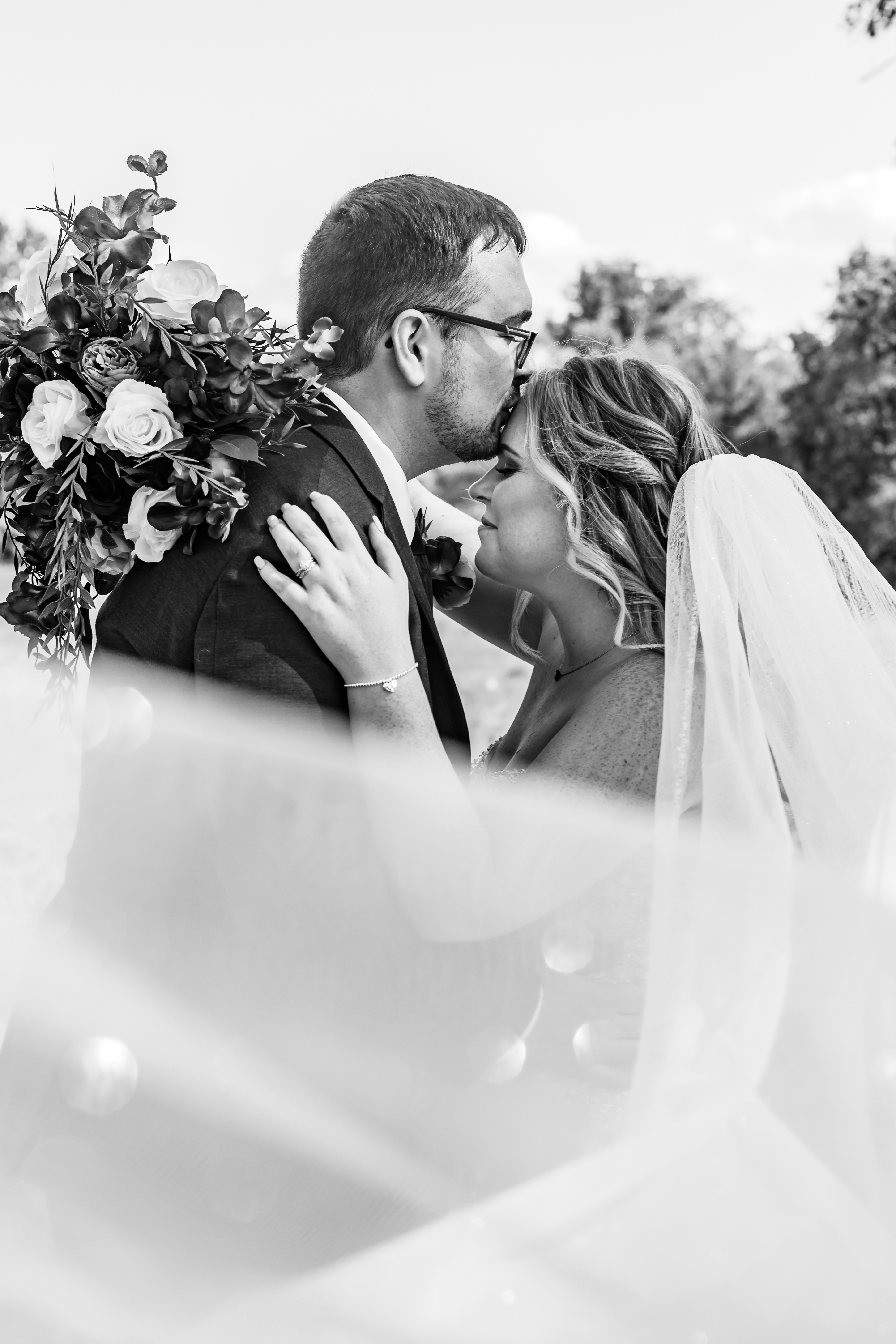 black and white portrait groom kissing bride on forehead