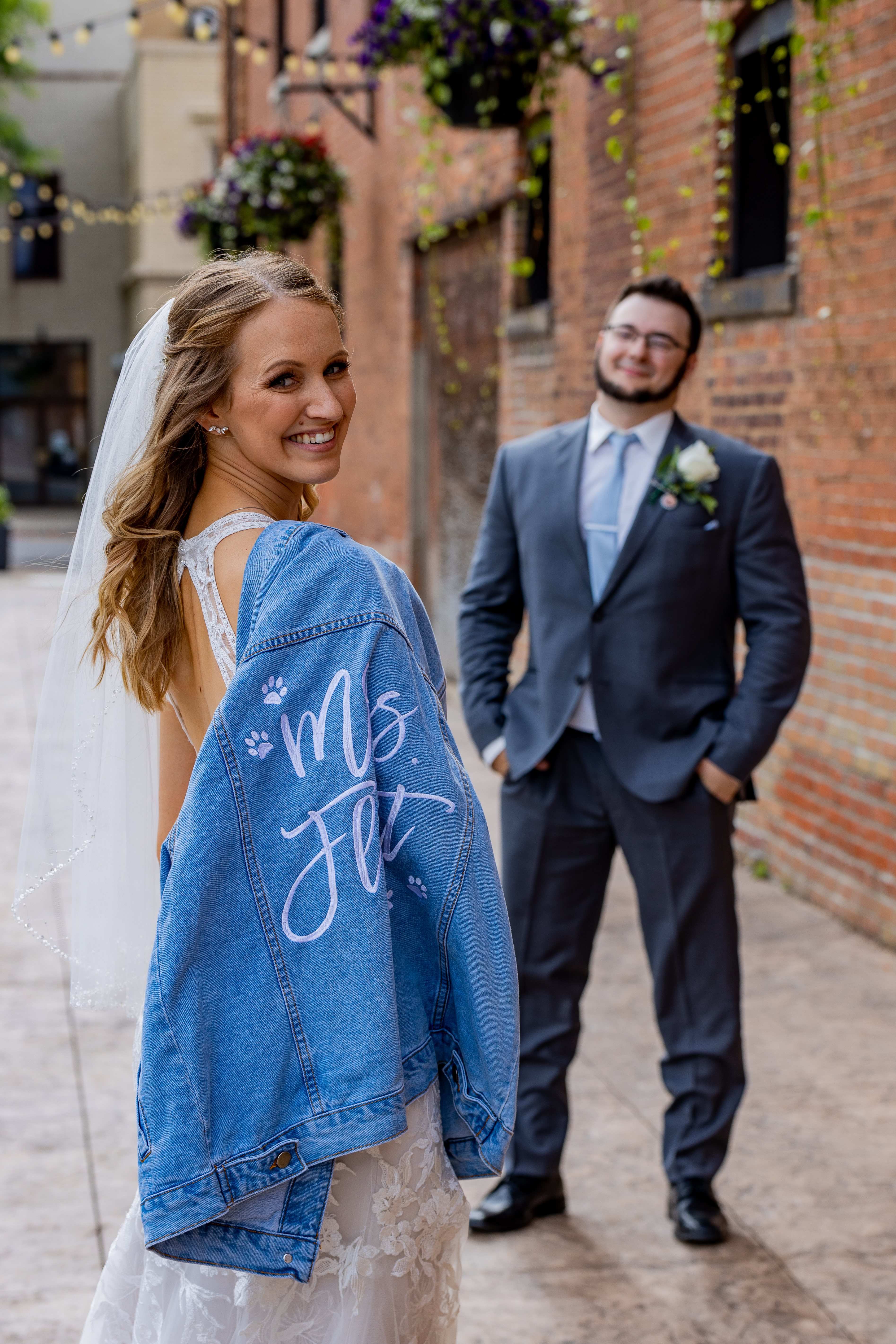 groom looking at bride who's holding personalized jean jacket over shoulder