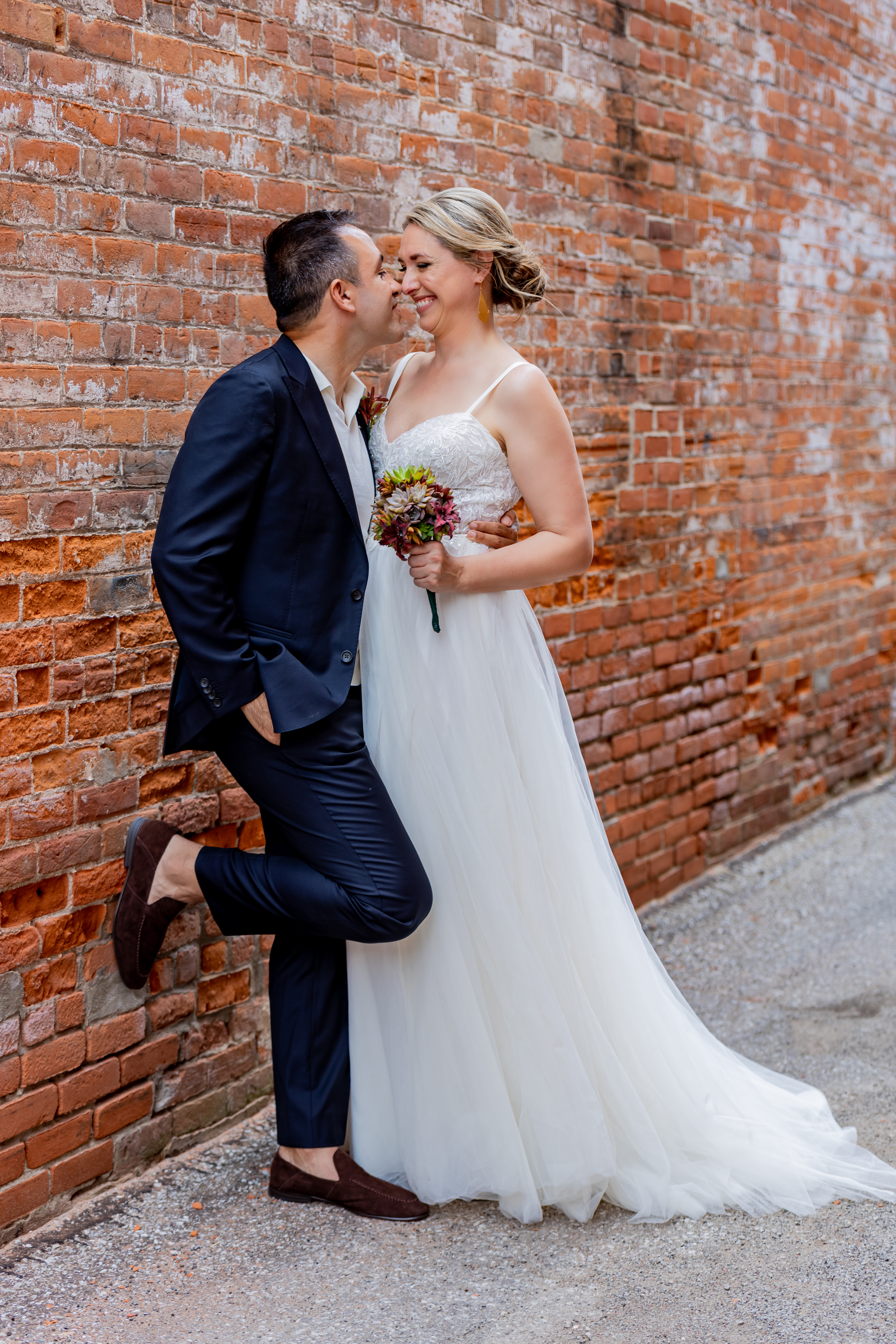 bride and groom leaning against brick wall