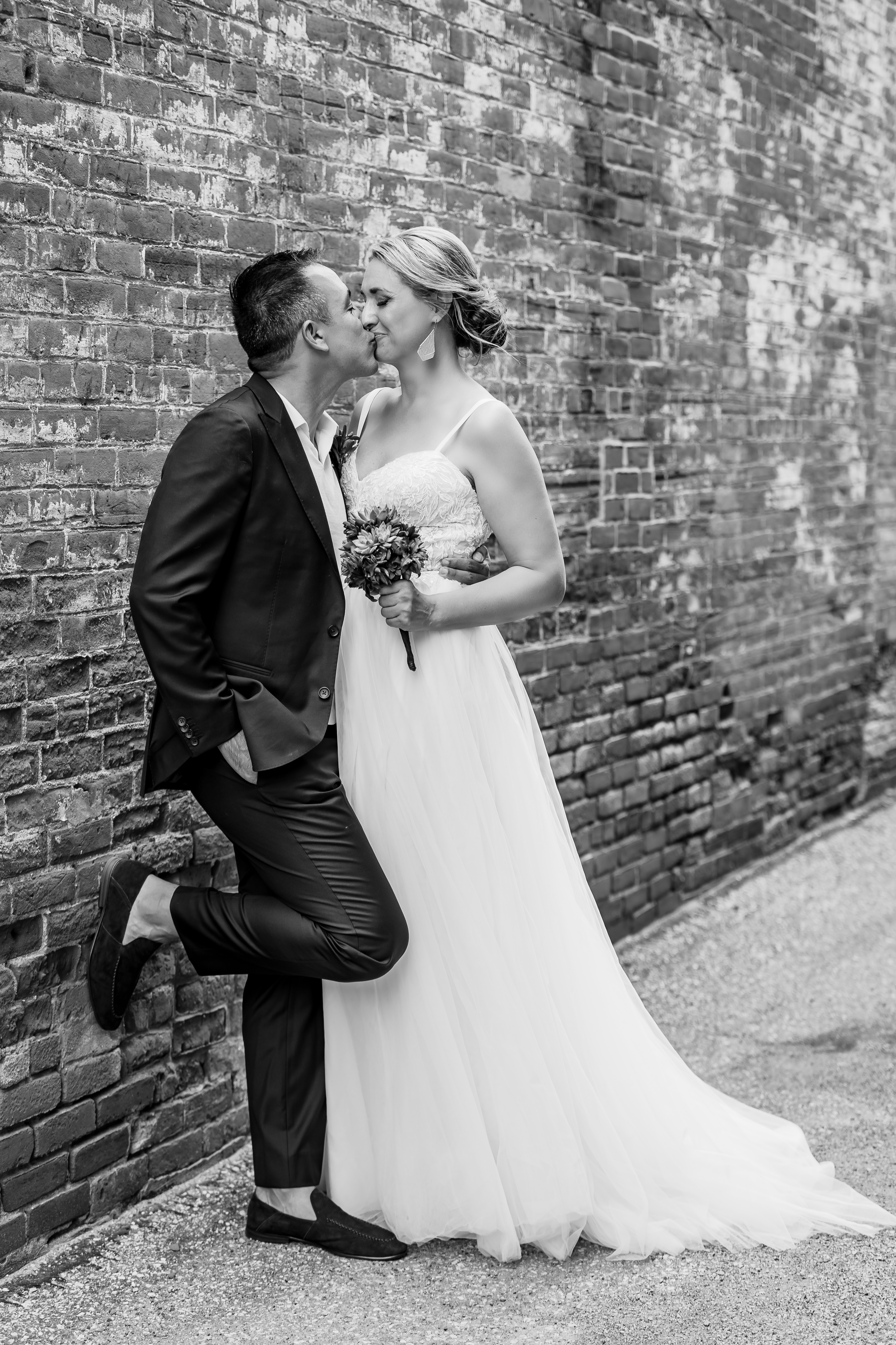 black and white portrait of bride and groom kissing next to brick wall