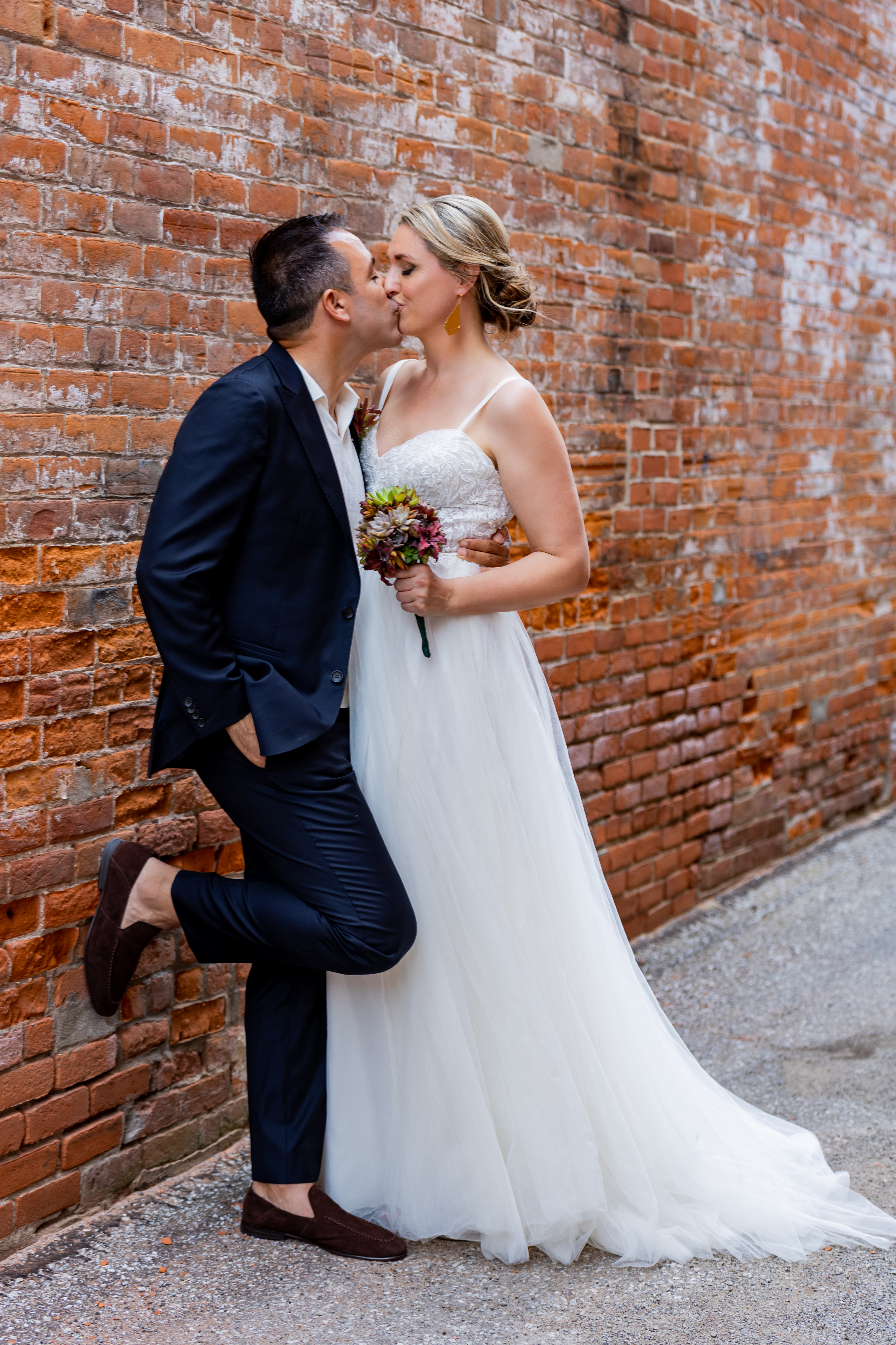bride and groom kissing against brick wall