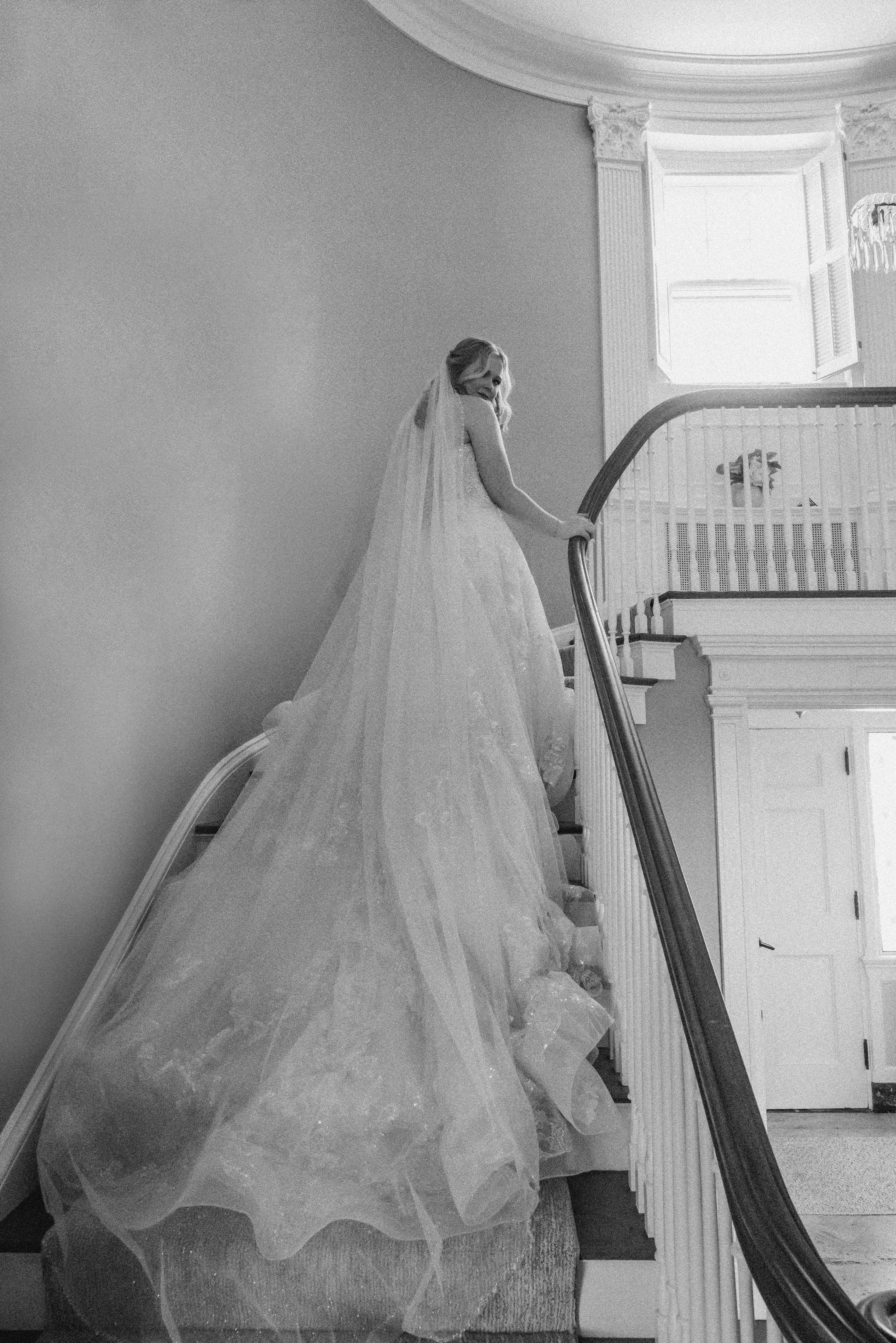 black and white portrait of bride walking up stairs with her veil and train behind her