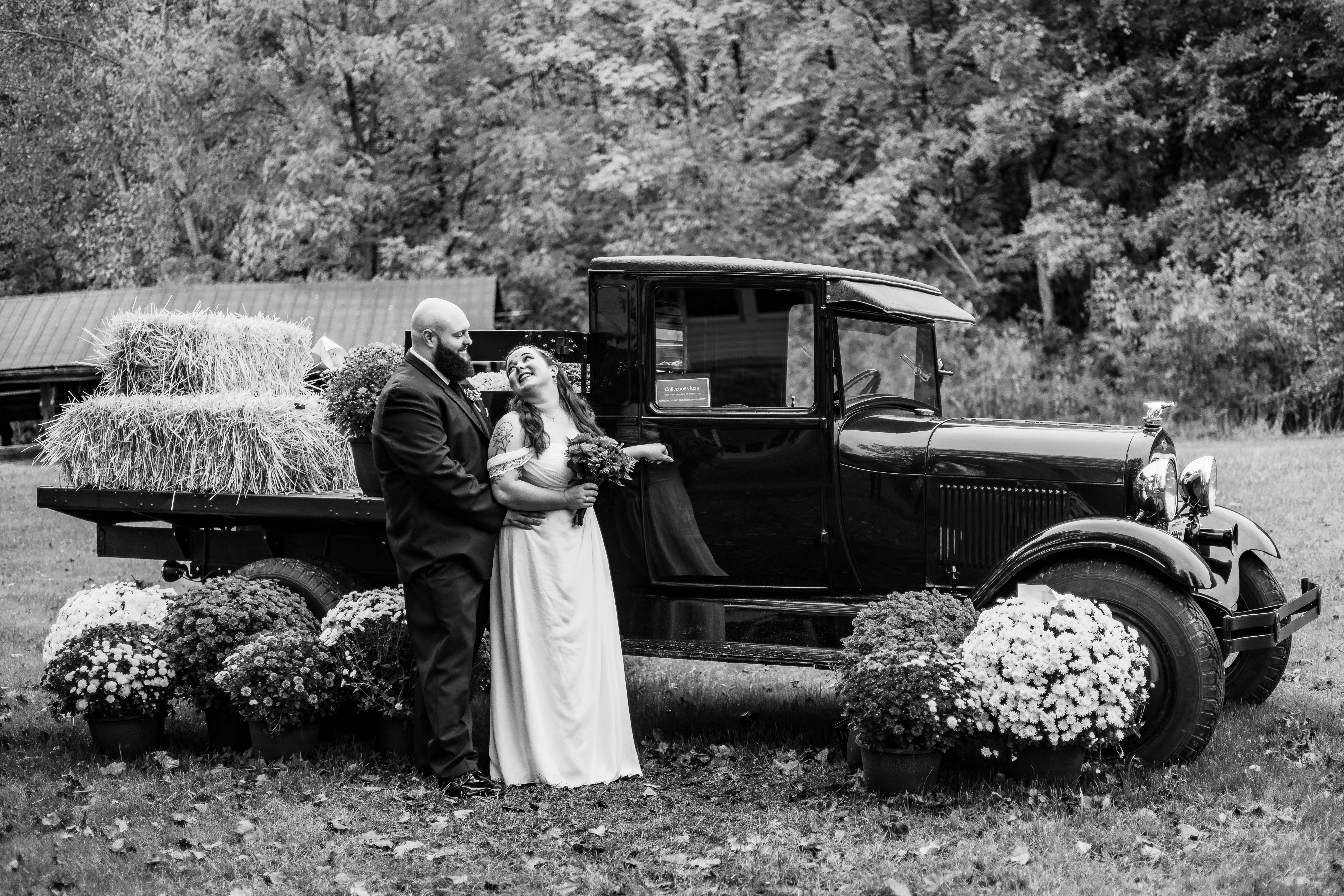 black and white portrait of bride and groom in front of antique truck