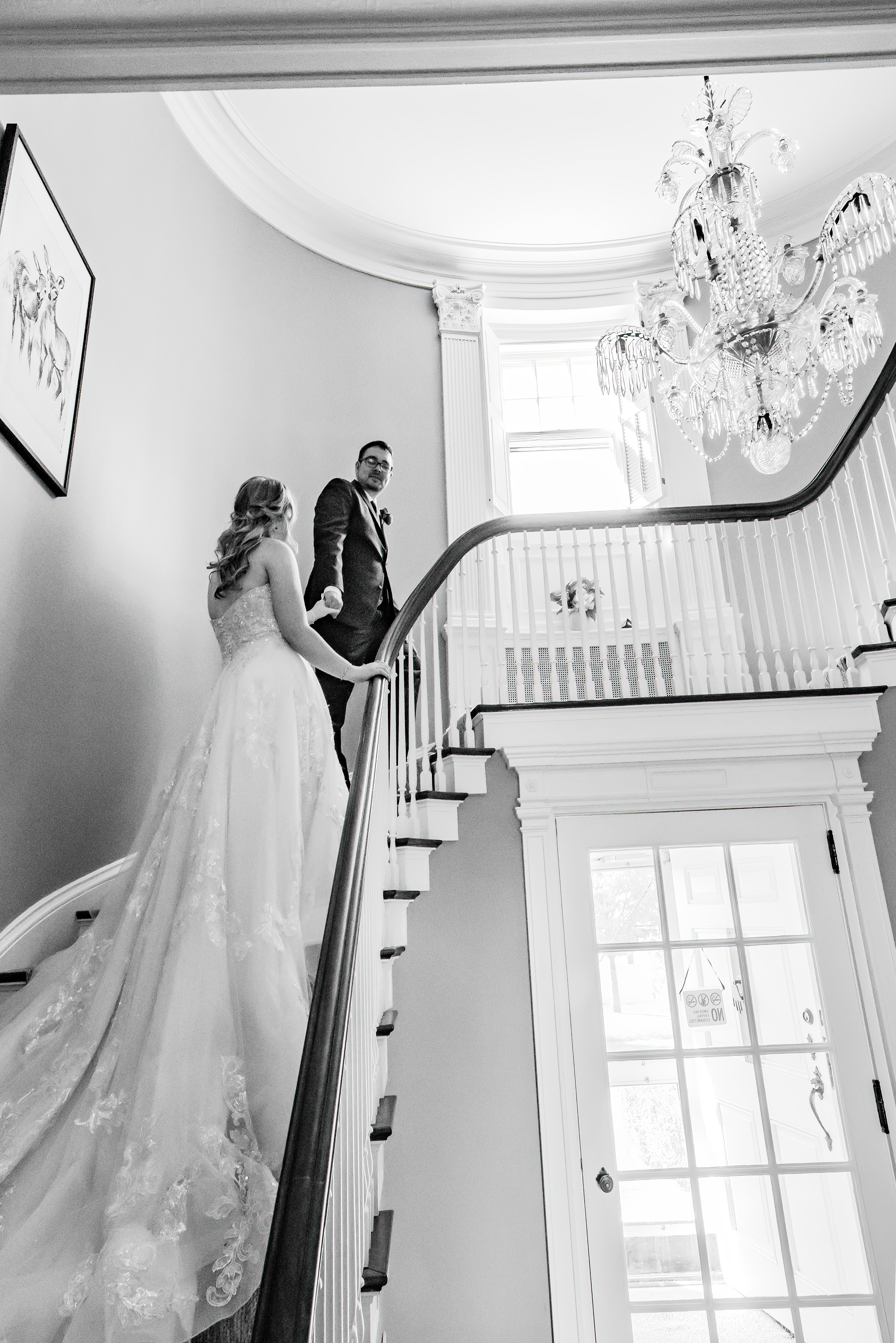 black and white wedding photo of bride and groom walking up stairs holding hands