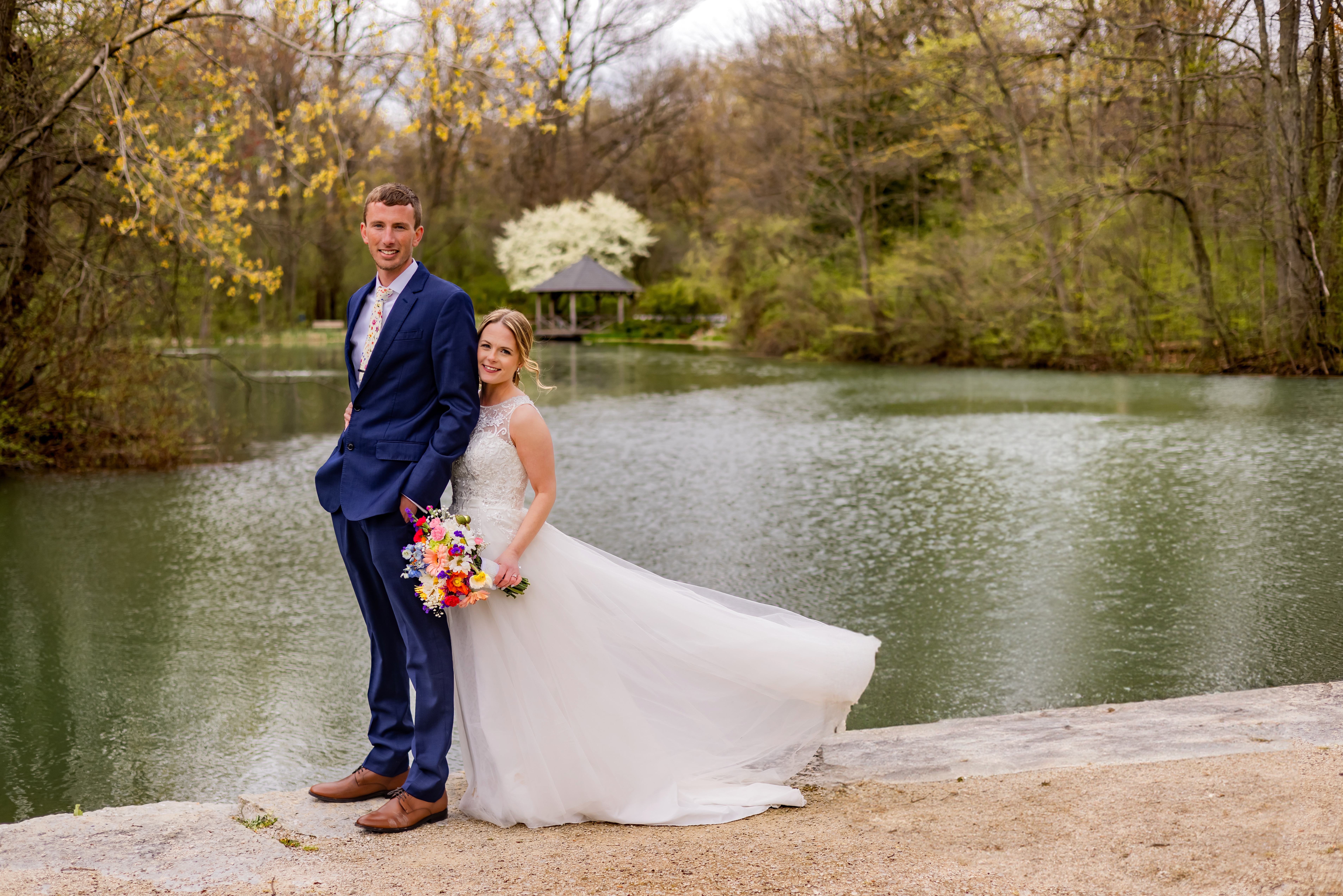 bride and groom standing next to pond