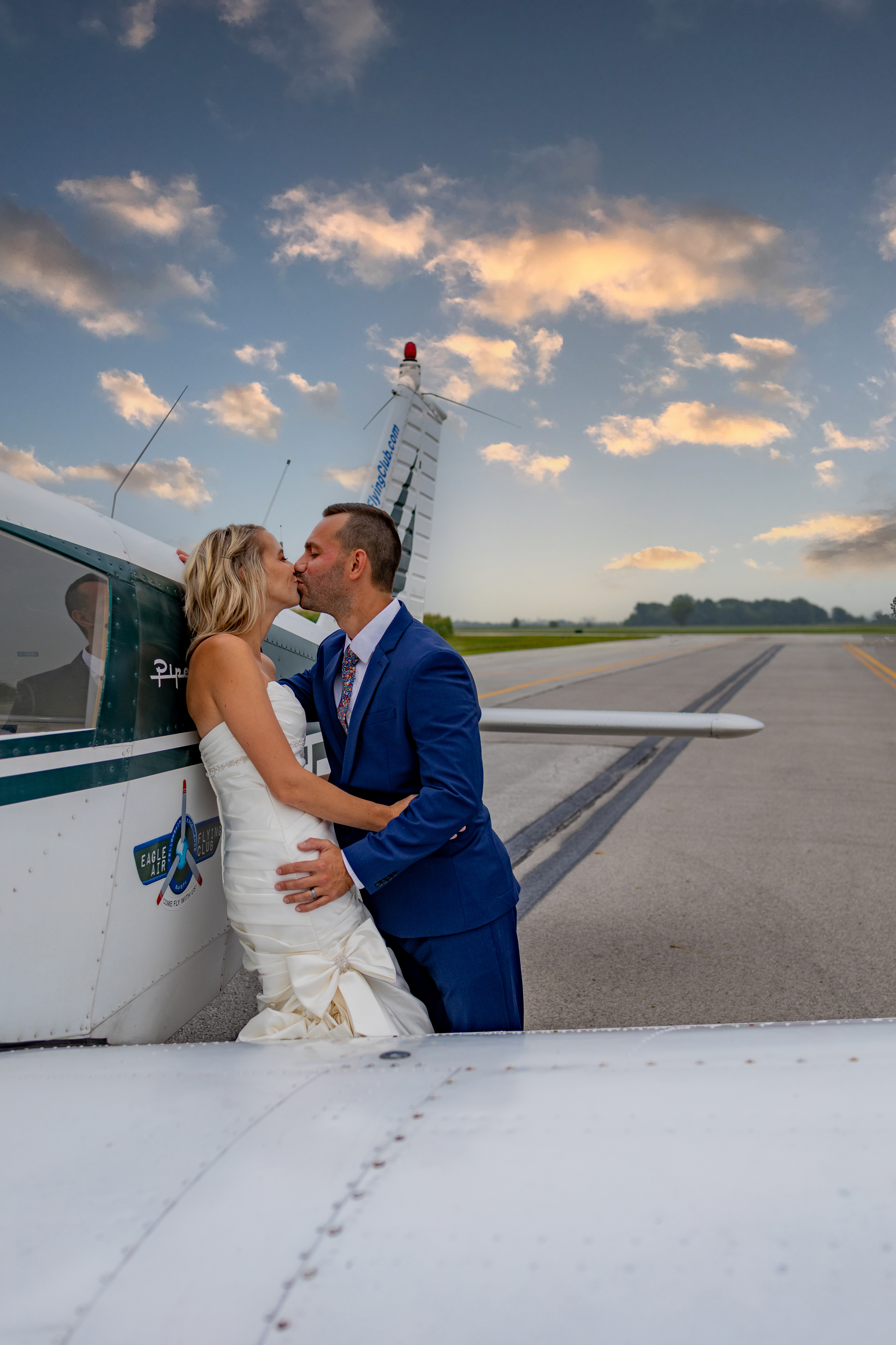 groom and bride kissing against airplane