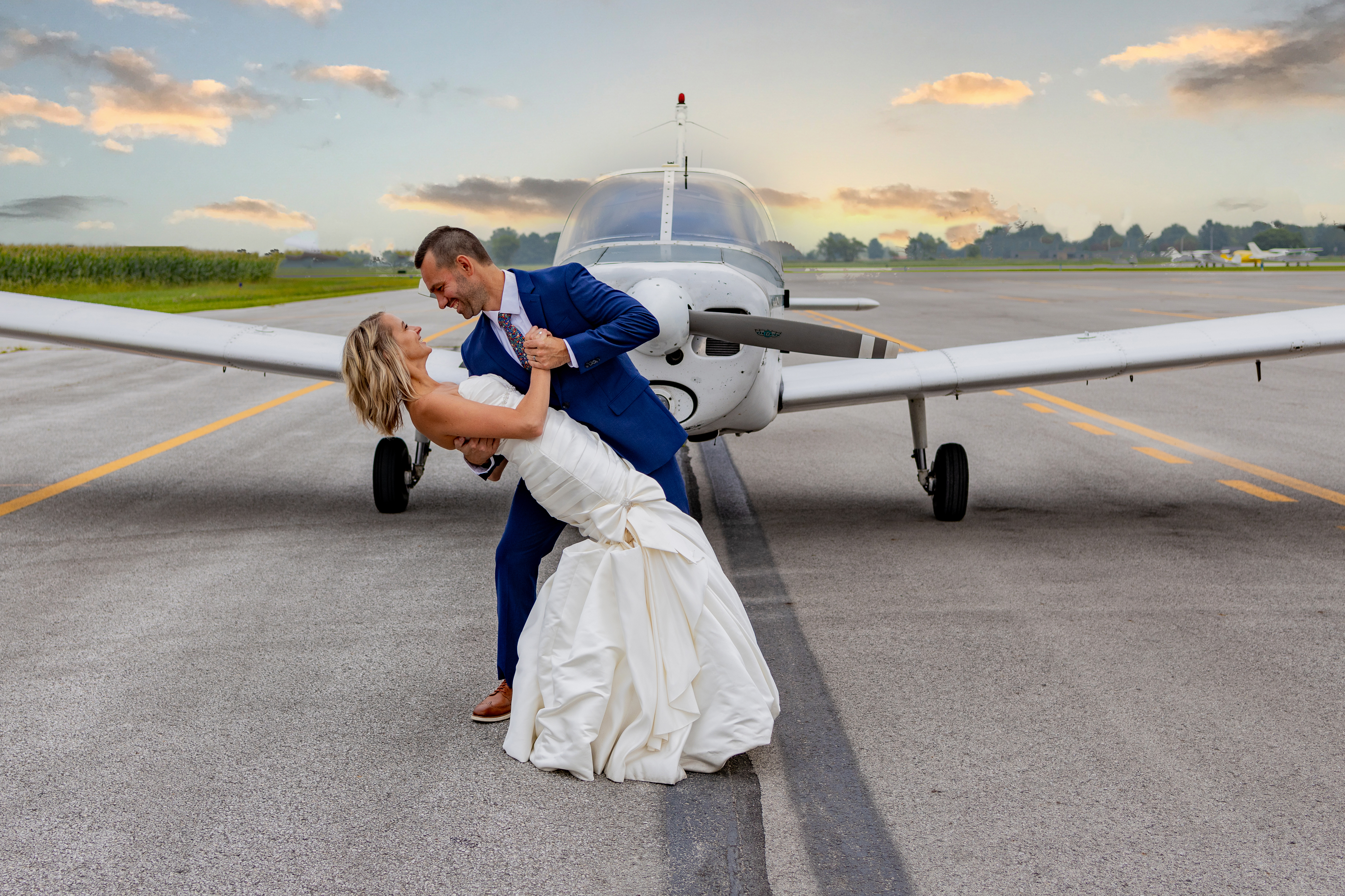 bride and groom on runway in front of airplane