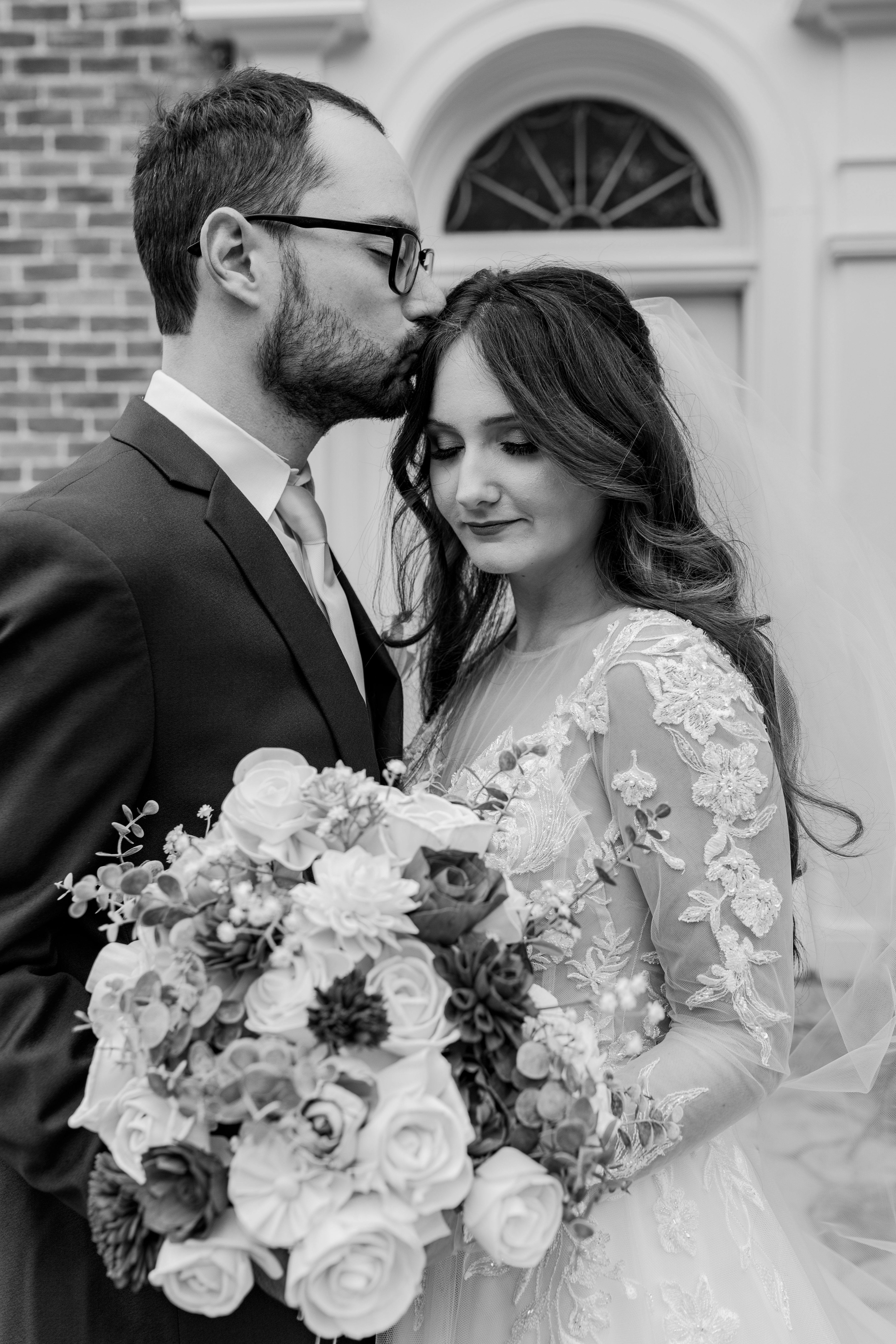 black and white wedding portrait of groom kissing bride's forehead