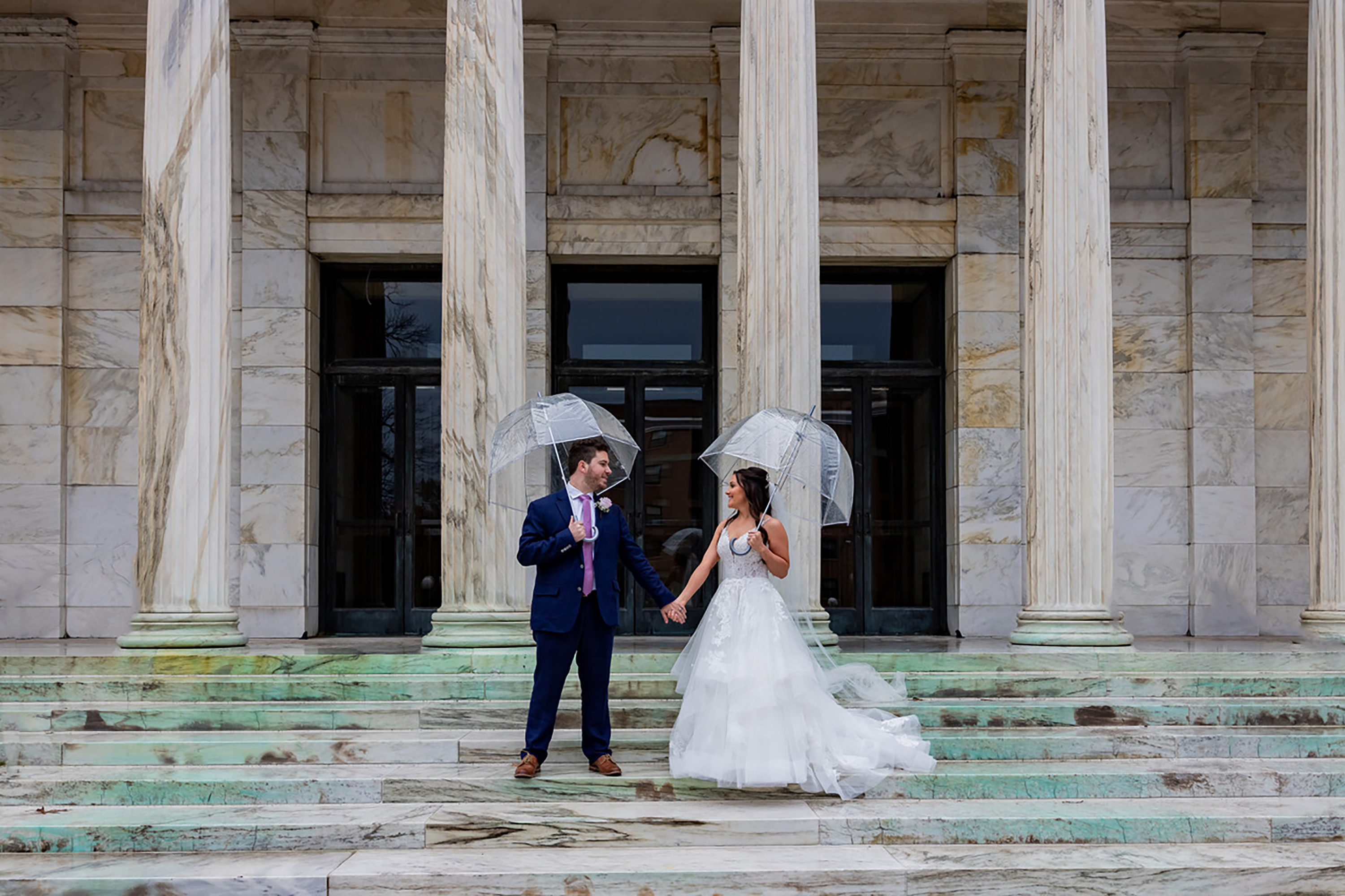 bride and groom holding clear umbrellas on venue steps