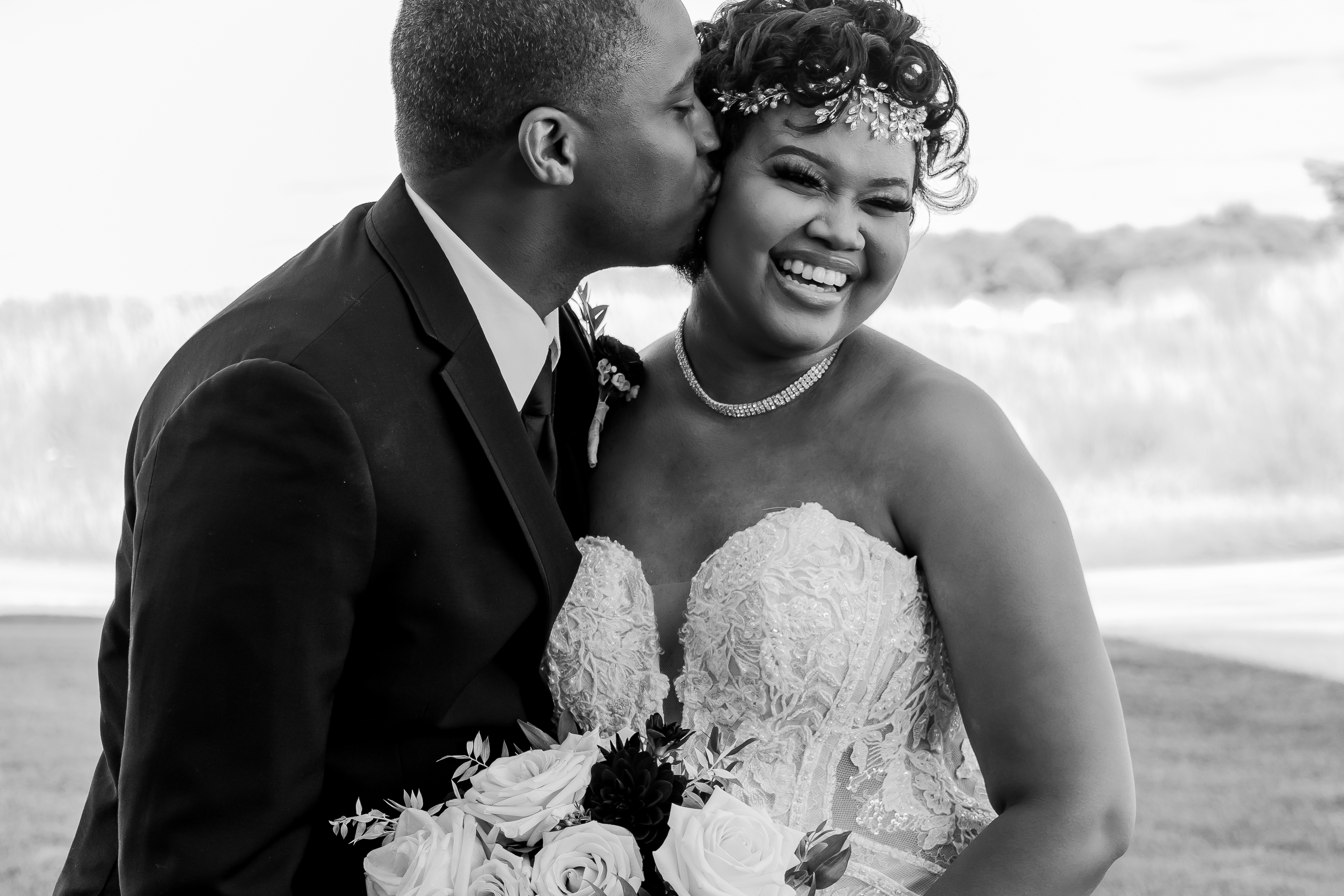 black and white portrait of groom kissing smiling bride on cheek