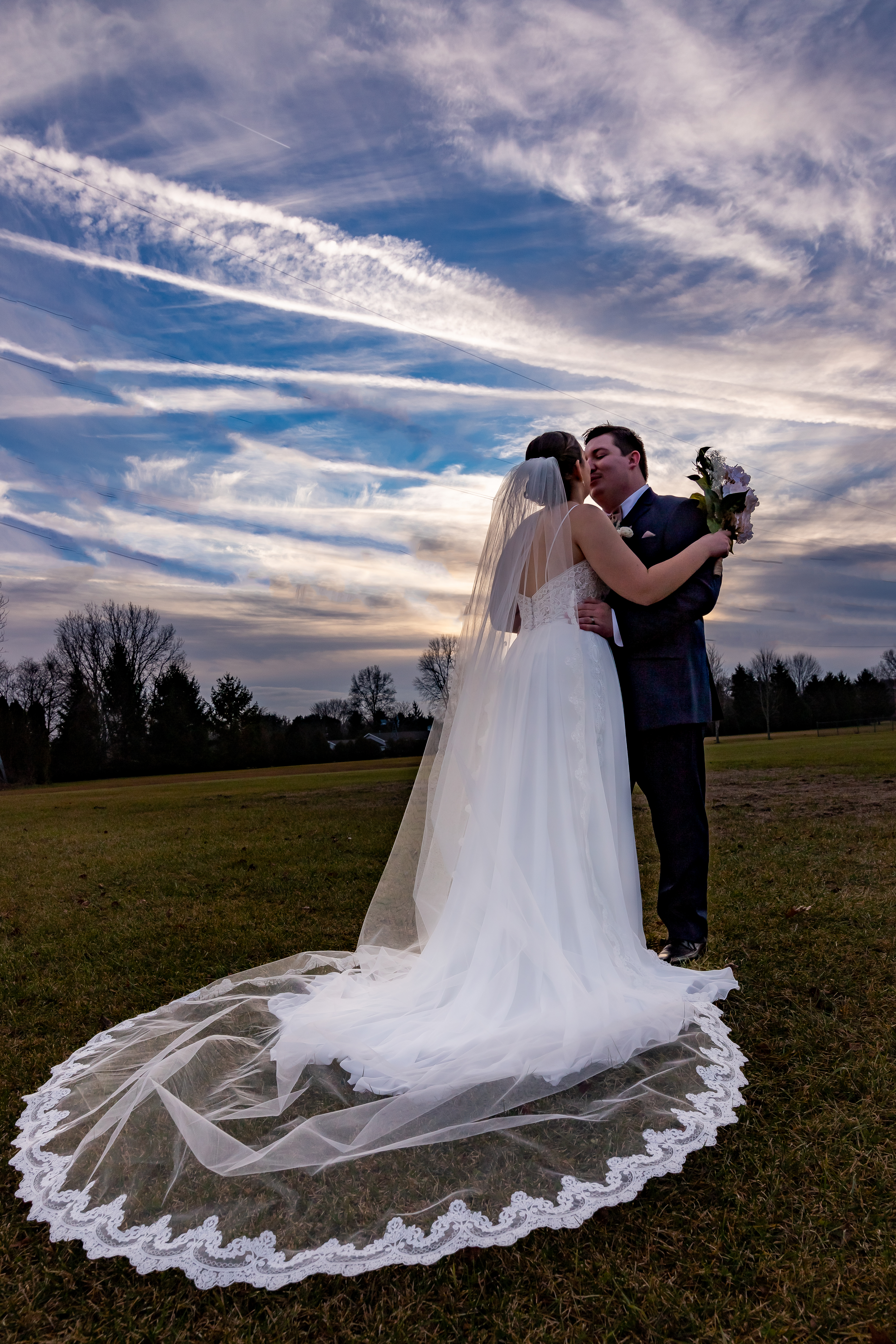 bride and groom kissing with bride's veil flowing behind them